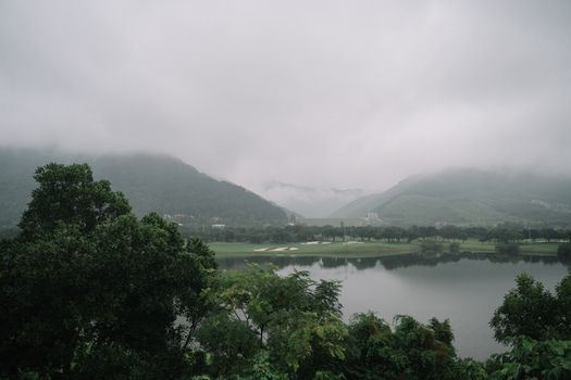 薄雾笼罩的宁静景观中，郁郁葱葱的山脉环绕着绿树成荫的湖泊