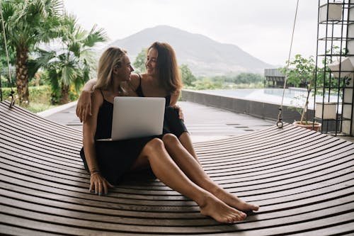 Macbookを見て木製のドックに座っている2人の女性