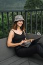 戴着豹纹帽、穿着黑色衣服的女人在户外用笔记本电脑工作