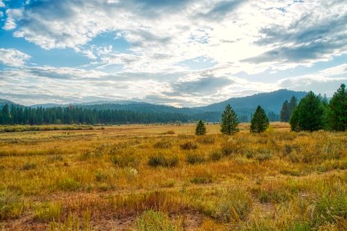 Free Expansive meadow with mountains and clouds creating a picturesque outdoor scene. Stock Photo