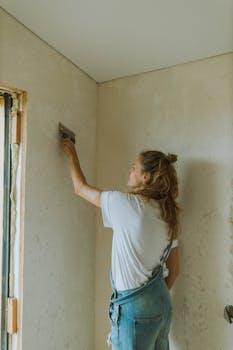 Adult woman plastering a wall indoors, focusing on home renovation activities.