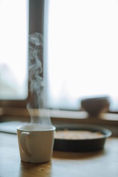 木桌上的窗口旁，蒸咖啡杯营造出舒适的室内气氛