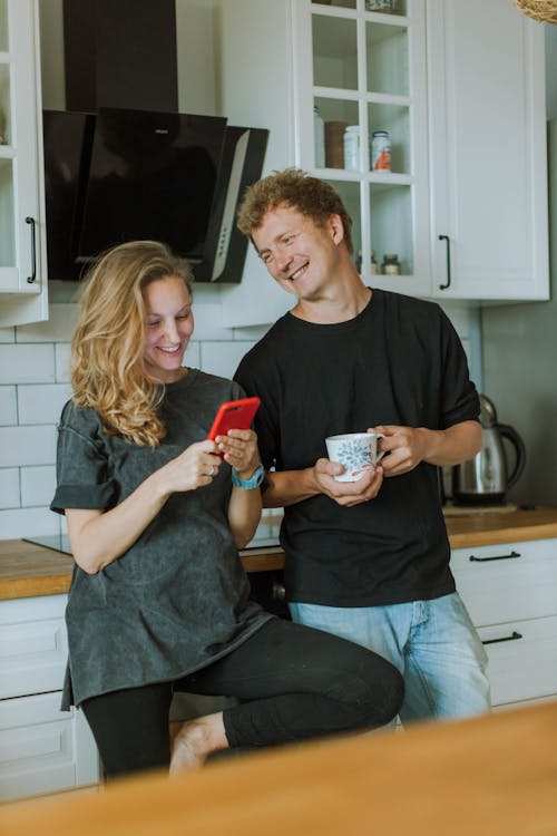 Woman in Gray Shirt Using a Smartphone and Man in Black Shirt Holding a Cup