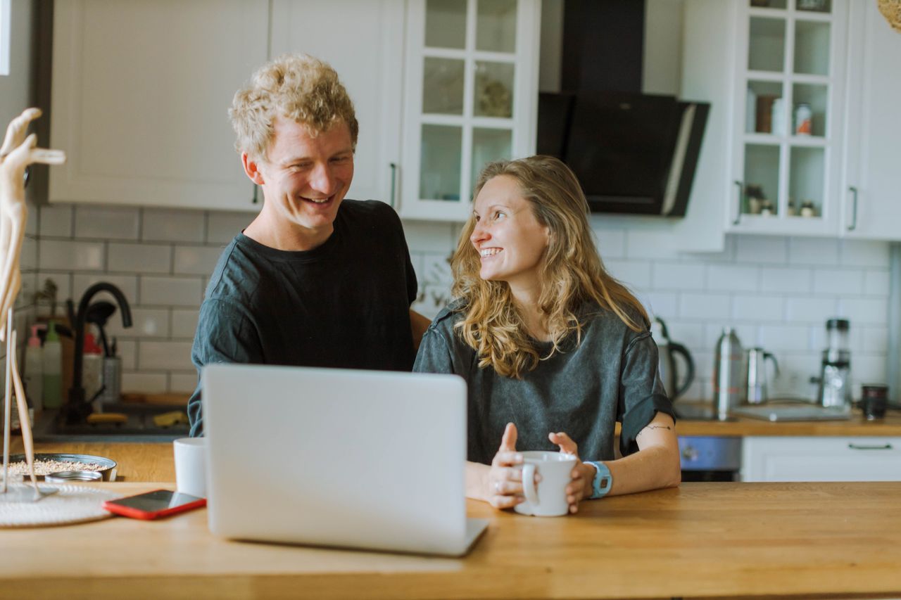 Smiling young couple reviewing their finances on a laptop at their kitchen table