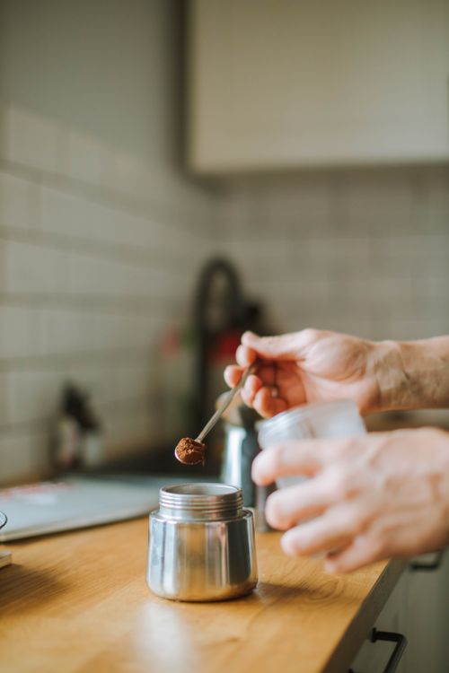 Free A person adding coffee grounds to a Moka pot on a wooden counter in a home kitchen. Stock Photo