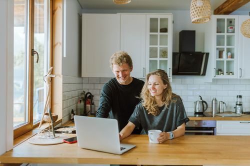 Free A happy couple enjoying coffee and using a laptop in their stylish, modern kitchen with natural light. Stock Photo