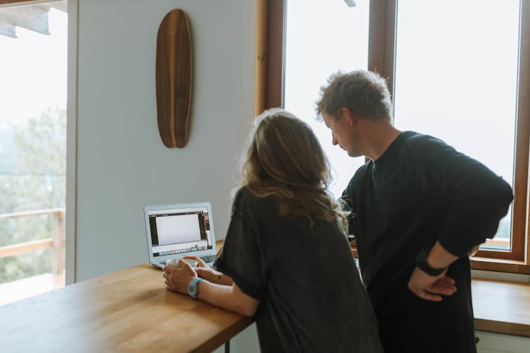 Man And Woman Using Laptop On Kitchen Counter Lif By Daylight From Window