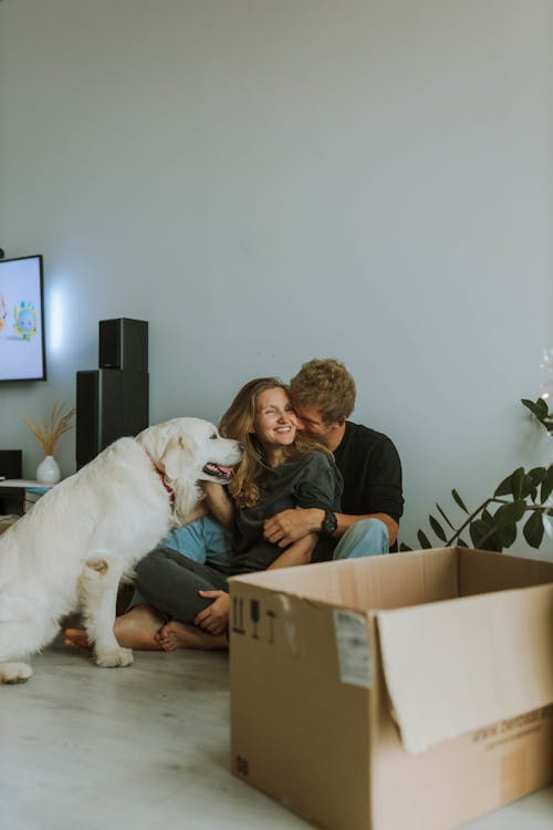Free Man Cuddles Woman while Sitting on the Floor Beside a Dog Stock Photo