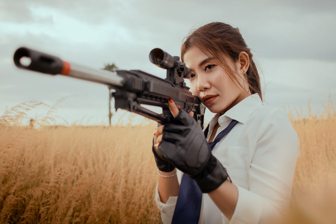 Serious Asian woman with rifle on grassy field