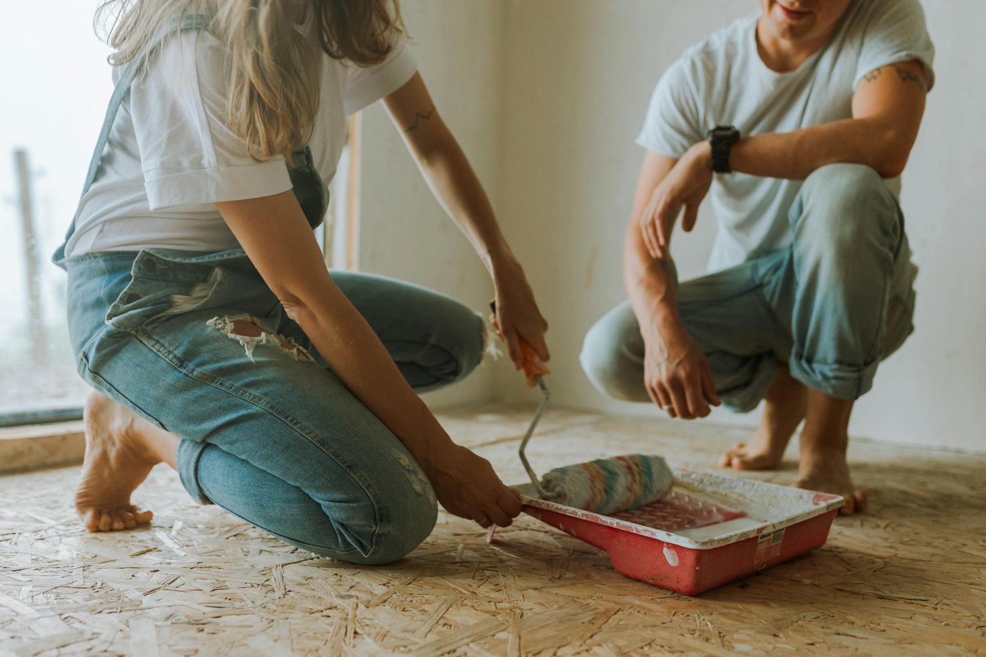 Young couple painting a room. They are kneeling on the floor, involved in a home renovation project.