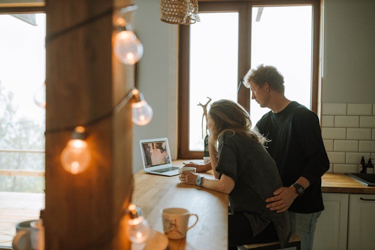 Man And Woman Looking At The Laptop On The Kitchen Counter