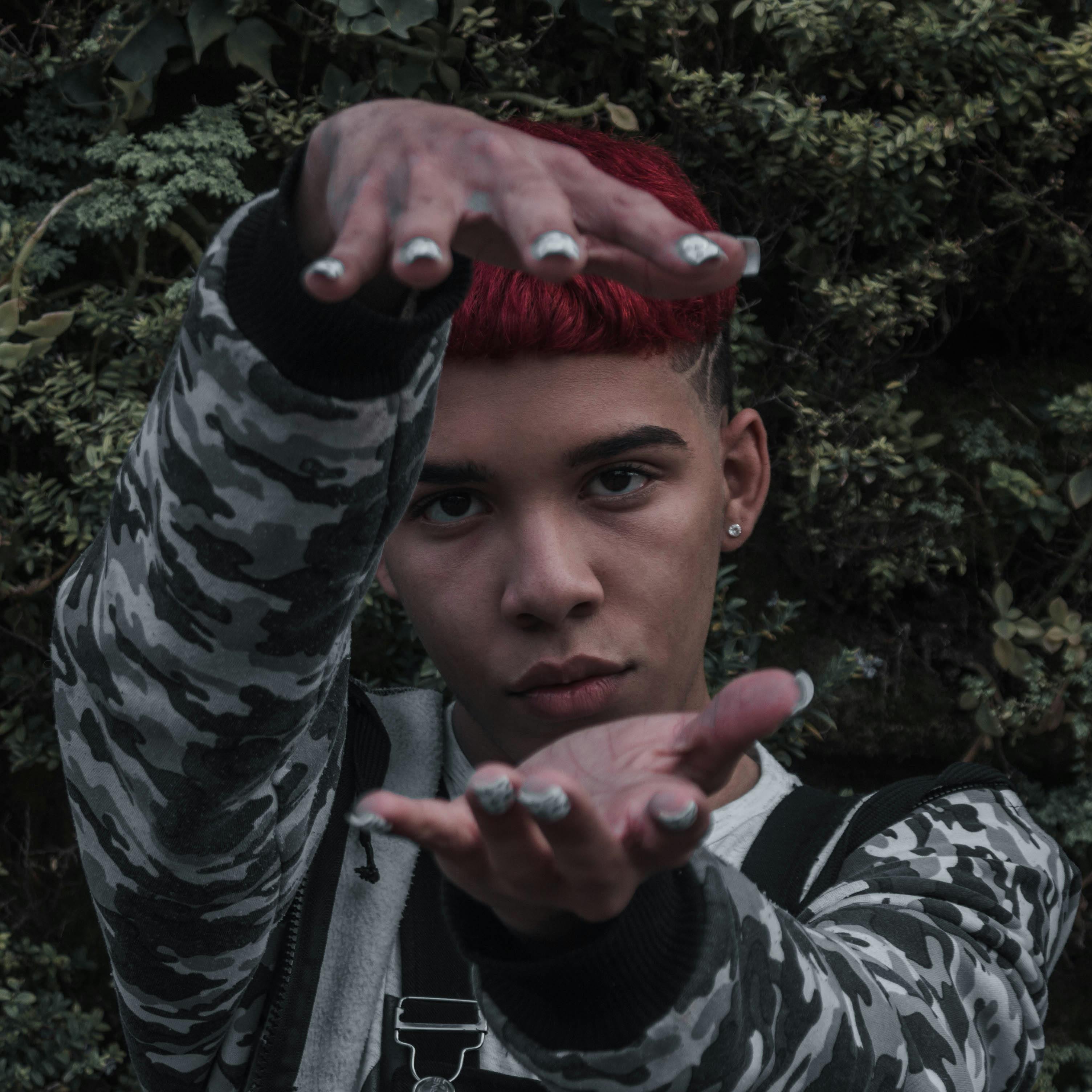 Artistic portrait of a person with red hair and a camouflage jacket, posing creatively outdoors.