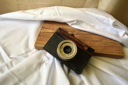 A rustic vintage camera placed on a wooden board with draped white fabric background.