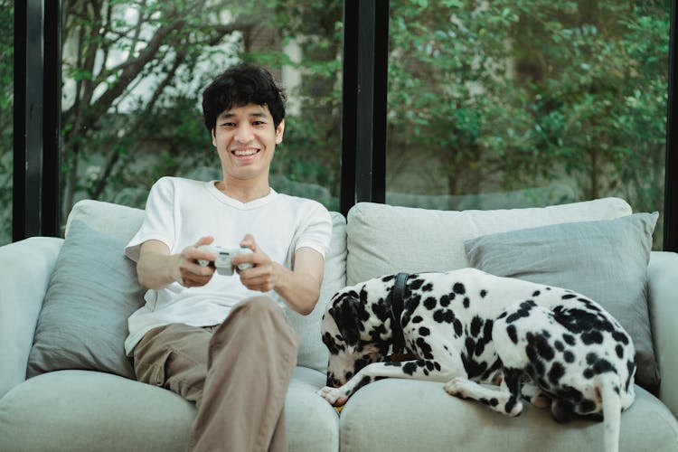 A Man Playing A Video Game Beside His Dog