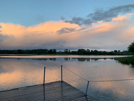 Peaceful sunrise scene with a pier reflecting on a lake, surrounded by serene nature.