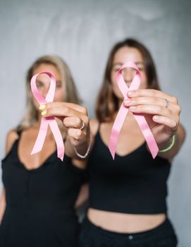 两名妇女手持粉红丝带，象征着对乳腺癌的认知与支持