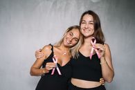 两名妇女手持粉红丝带，微笑着支持乳腺癌防治宣传