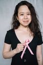 女人手持一条象征乳腺癌意识的粉红色丝带，微笑着