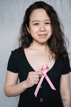 女人手持一条象征乳腺癌意识的粉红色丝带，微笑着