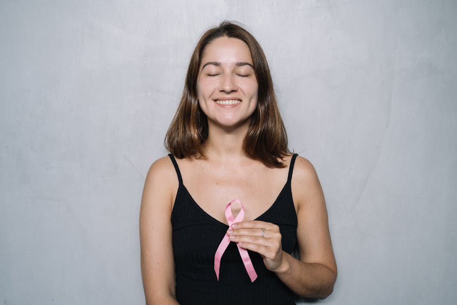 A smiling woman with eyes closed holds a pink breast cancer awareness ribbon, symbolizing hope and h