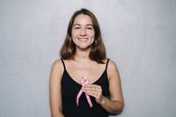 一位微笑的女性手持粉红丝带，在中性背景下象征乳腺癌意识