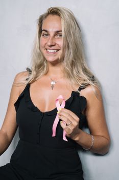 女人手持一条粉红色的丝带，微笑着，象征着对乳腺癌的认识和支持