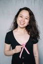 一位手持粉色丝带的女性微笑着，象征着对乳腺癌的关注