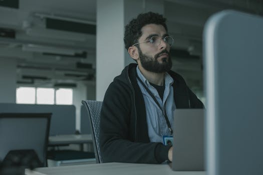 Man with eyeglasses working at a desk in an office setting, focused and engaged.