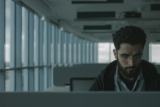 一个戴着眼镜、留着胡须的男人在一间有大窗户的现代办公室里工作