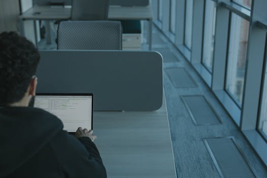 Man working on a laptop in a modern office setting, using advanced technology.