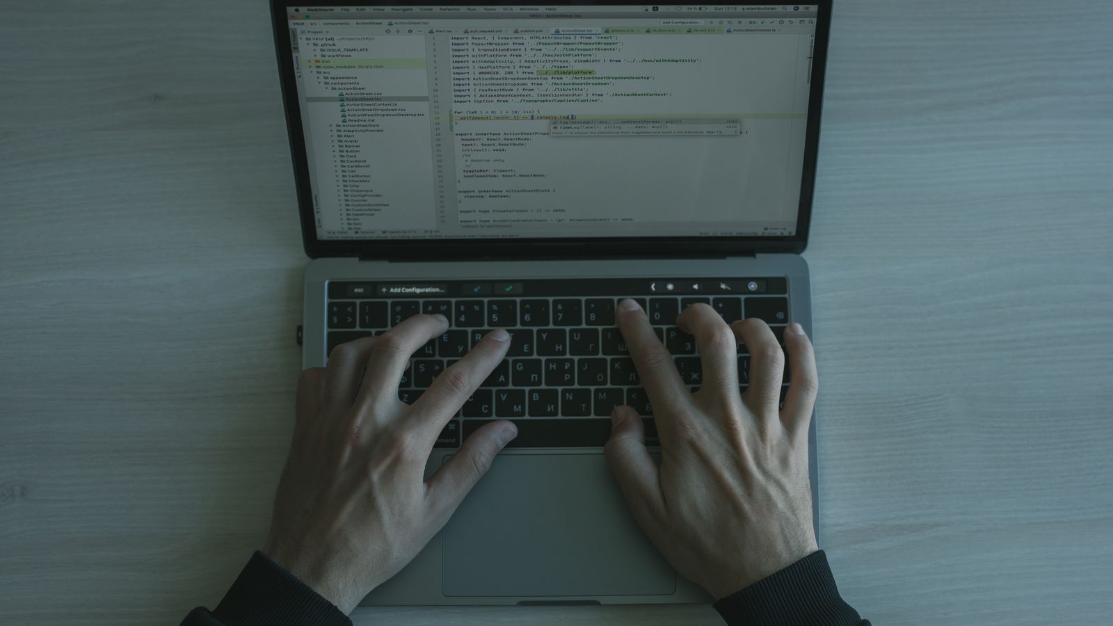 Hands typing on a laptop beside a latte and a small vase of flowers near a window