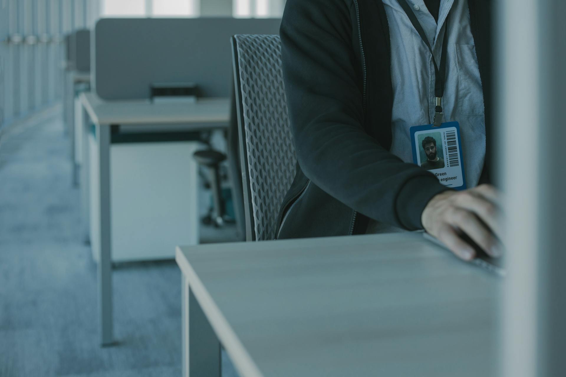 Close-up of a man working in a modern office setting, wearing an ID badge.