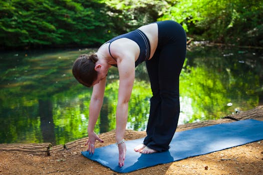 Woman in activewear performing yoga outdoors by a tranquil pond in a lush park setting.