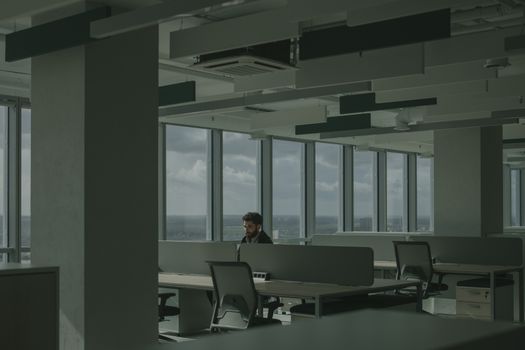 A man works alone in a spacious, modern office with large windows and natural light.