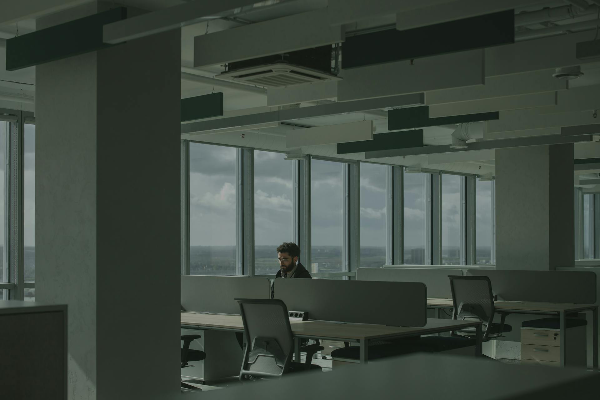 A man works alone in a spacious, modern office with large windows and natural light.