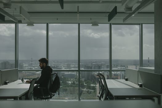 A man working on a laptop in a contemporary office with a large cityscape view.