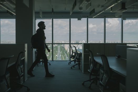 一个男人的剪影走过一间有着大窗户和城市景观的现代化办公室内部