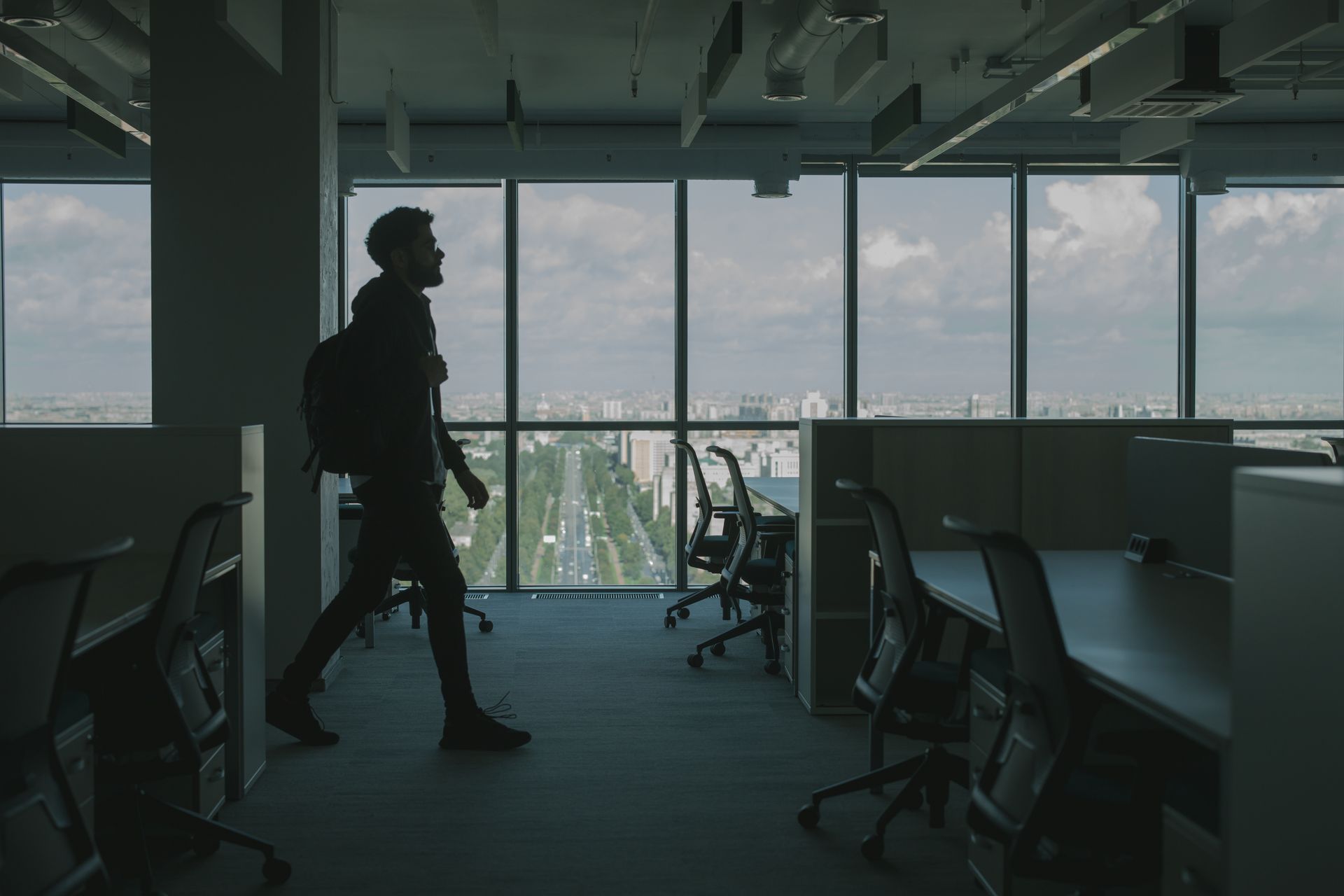 Silhouette of a man walking through a modern office interior with large windows and an urban city view.