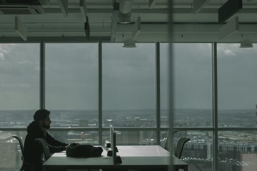 Man in modern office setting at a desk overlooking a cityscape through large windows.