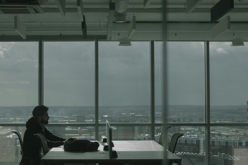 Free Man in modern office setting at a desk overlooking a cityscape through large windows. Stock Photo