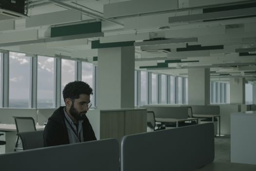 Man in eyeglasses working alone in a spacious modern office with large windows.