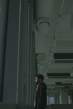 在一个现代化的办公空间里，一个穿着黑色连帽衫的男人站在窗户旁沉思
