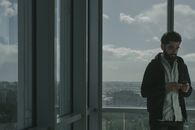 一名男子站在现代办公室的玻璃窗旁，用智能手机映出窗外的城市景观