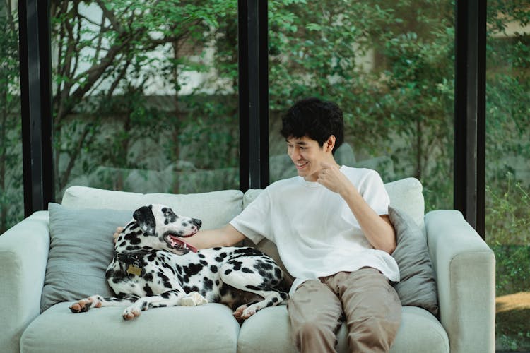 A Man Sitting On The Couch With His Dog