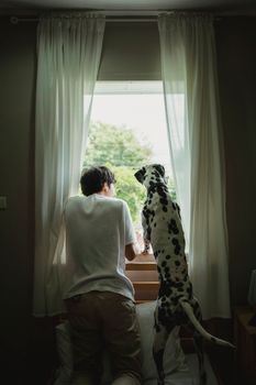 A man and his Dalmatian dog gaze out an open window together.