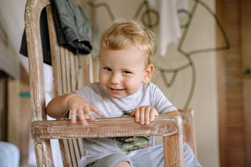 Free Charming young boy sitting on a chair with a playful expression indoors. Stock Photo