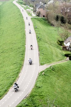 Aerial view of motorcyclists riding through a picturesque countryside road surrounded by greenery.