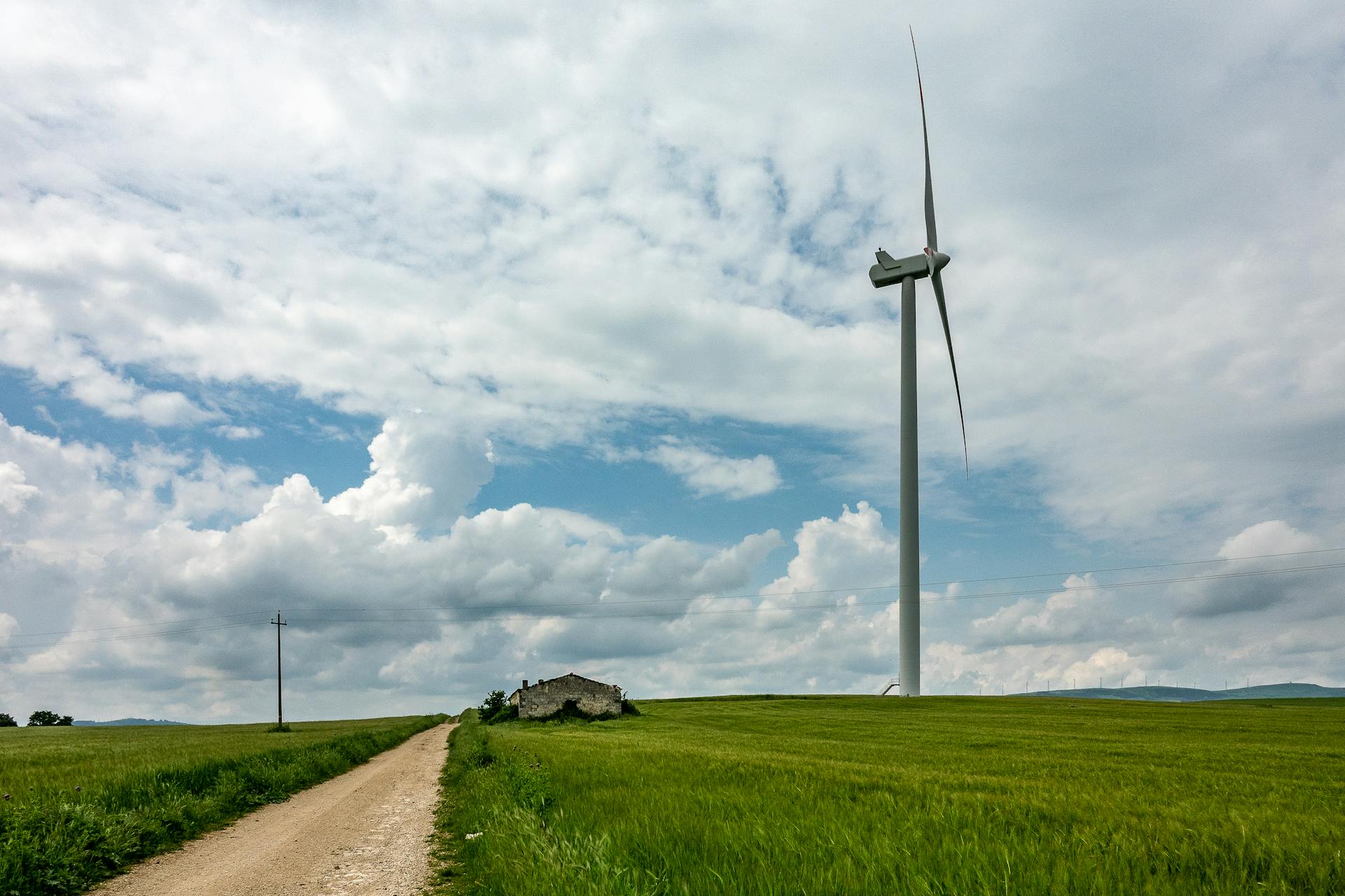 A lone wind turbine stands tall amidst lush green fields under a cloudy sky, symbolizing renewable energy.