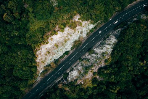 Free Drone view of cars driving on asphalt roadway between green trees on rocky highlands Stock Photo