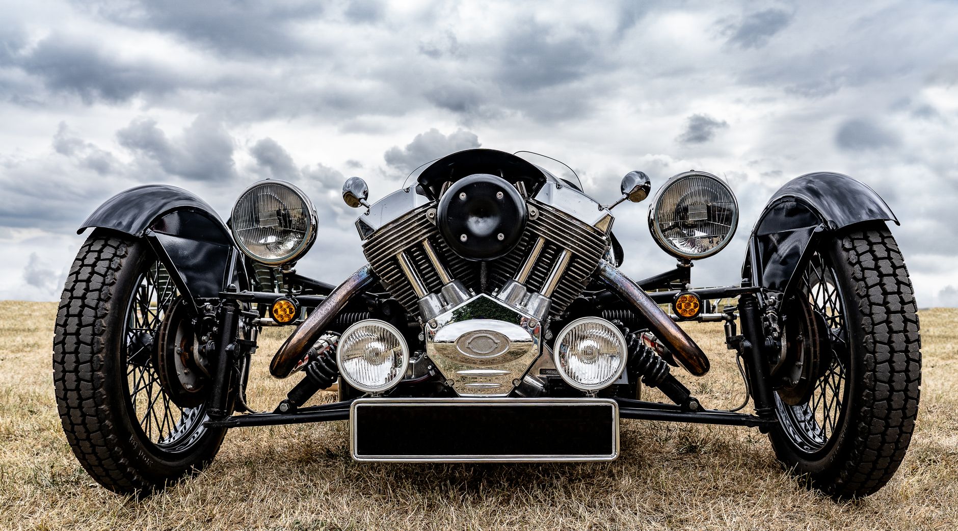 Front view of a vintage car with large wheels on grassland under a dramatic cloudy sky.
